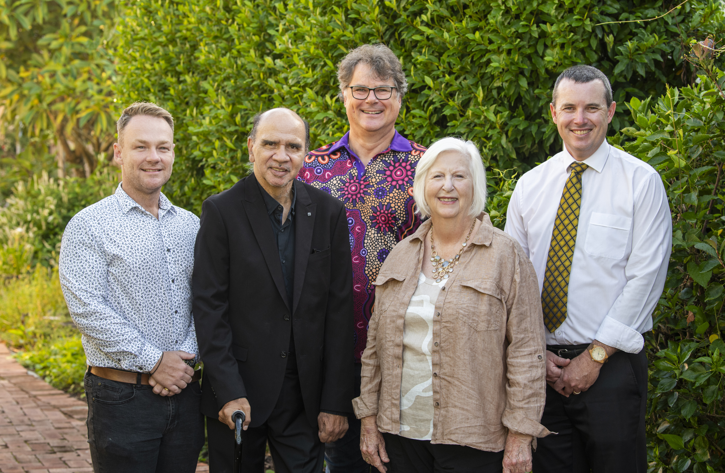 Five people standing in front of green foliage. From left to right: a man in a patterned white shirt, a man in a black suit with a walking stick, a person in a vibrant purple patterned shirt, a woman in a tan jacket with white hair and statement necklace, and a man in a white shirt with yellow tie.

From left to right stand Joshua Craig, Darren Kershaw, Leon Ankersmit, Vicki St Lawrence and Timothy White.